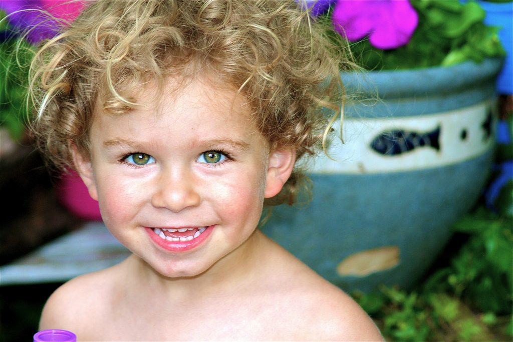 Blonde curly-haired baby boy sitting amongst the flowers