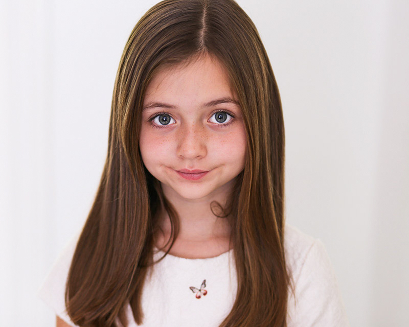 Child actress in white dress and long hair smiling into the camera