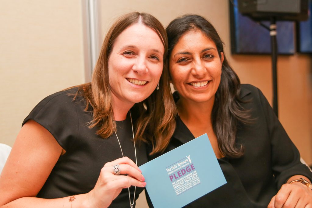 Two women sitting together at table at event holding pledge card