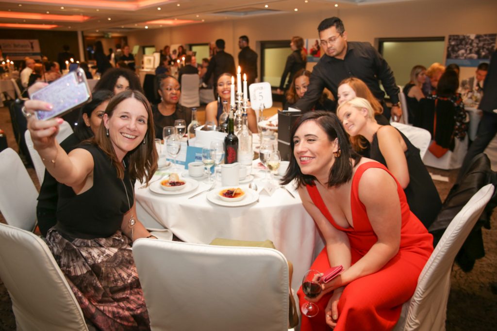 Women sitting around table at gala party taking selfies