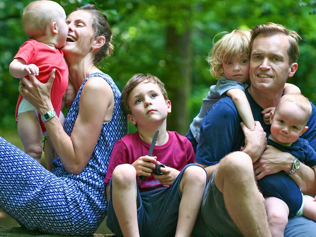 A family sitting together on a tree trunk in the woods in North London. Boy in the middle holding a toy