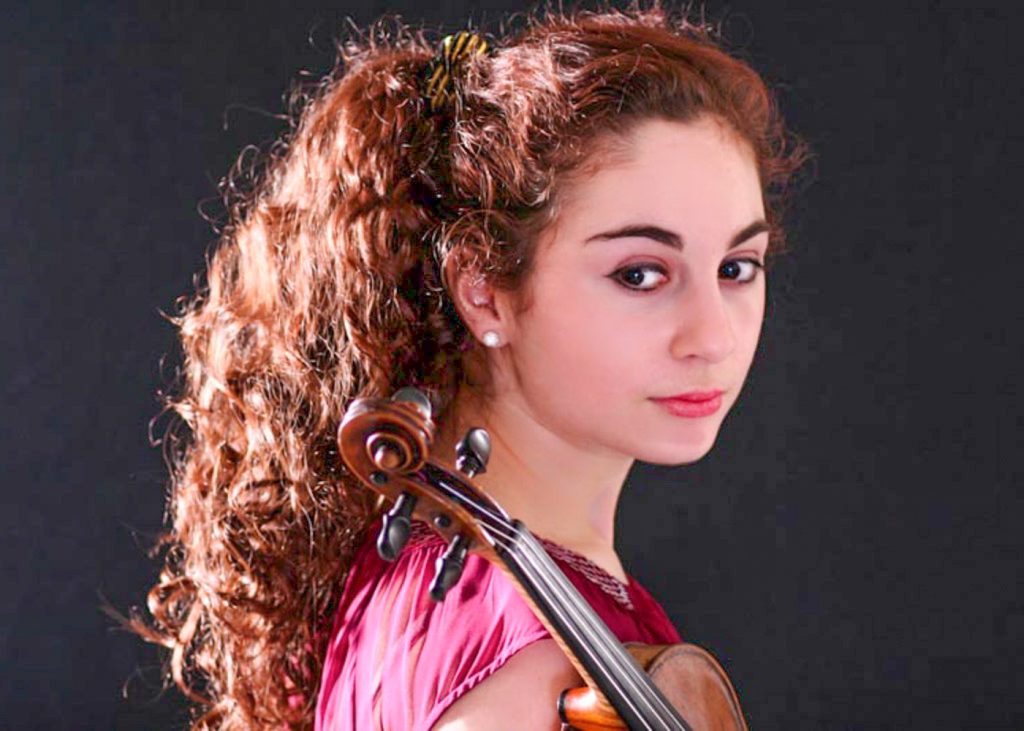 Headshot of young lady with long curly brown hair holding violin