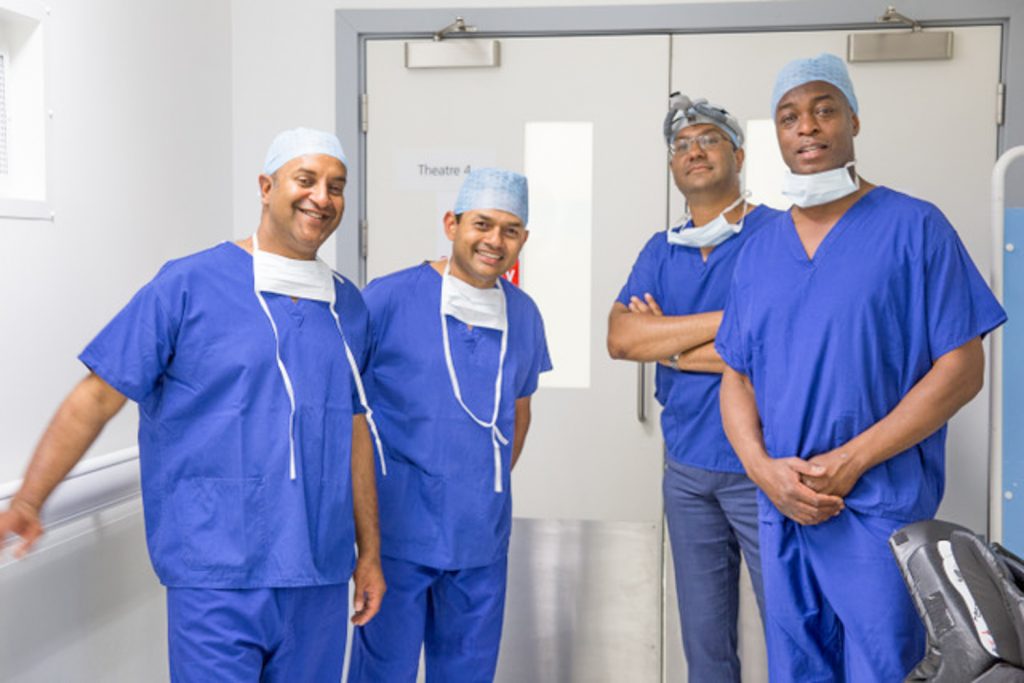 Photograph of four surgeons in scrubs standing outside theatre