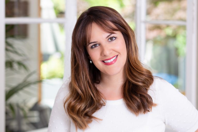 Smiley woman brown hair white top with garden in background