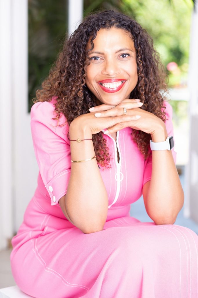 Pretty woman with long curly hair and wearing pink dress looking into camera with big smile