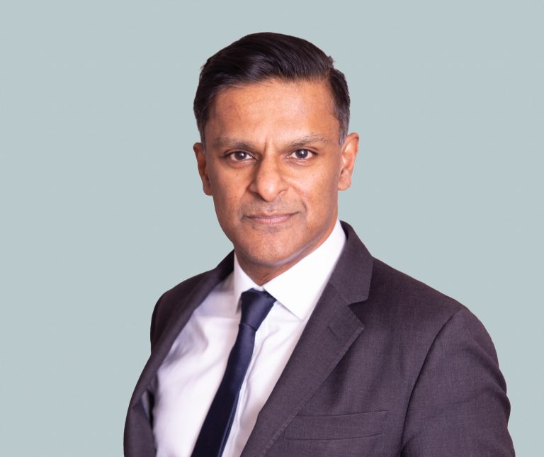 Smart man in dark suit staring into camera with blue background