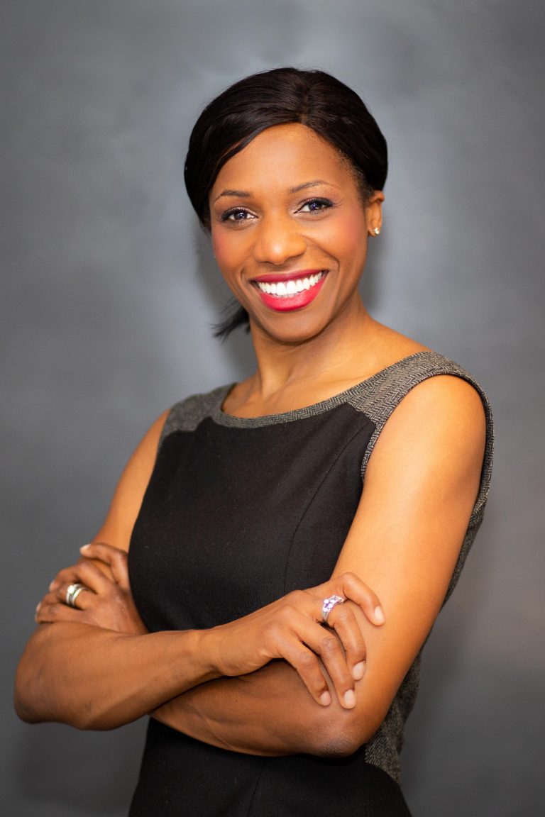 Black woman smiling into the camera with grey background