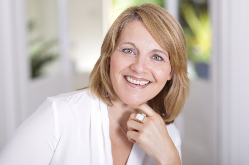 woman smiling into camera in white shirt with French doors and garden in background